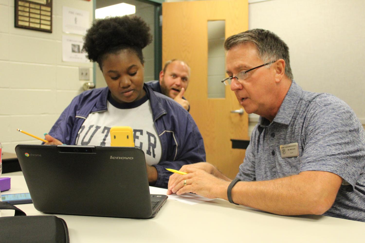 Working a full work day Monday through Thursday in the math office, retired math teacher Mike Slack dedicates his extra time to PM students who need additional math help. Students work with him in order to improve their standardized math test scores. Above, Slack helps junior Brooklyn Sanders in Algebra (Photo by Alexis Lee).